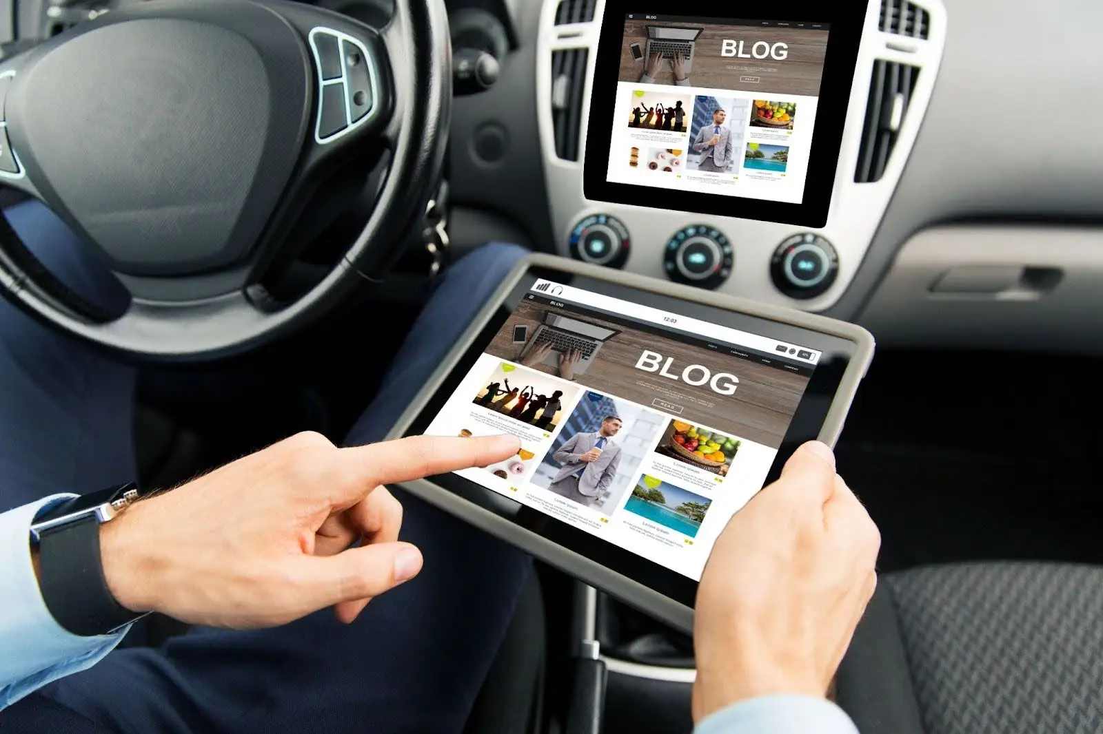 A person in a car uses a tablet displaying a blog webpage, with the same blog shown on the car&rsquo;s dashboard screen. The car interior and steering wheel are visible.