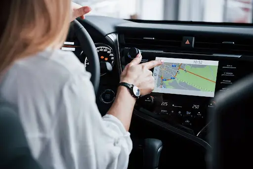 A person sitting in a car uses the touchscreen navigation system on the dashboard, with a digital map and directions displayed on the screen.