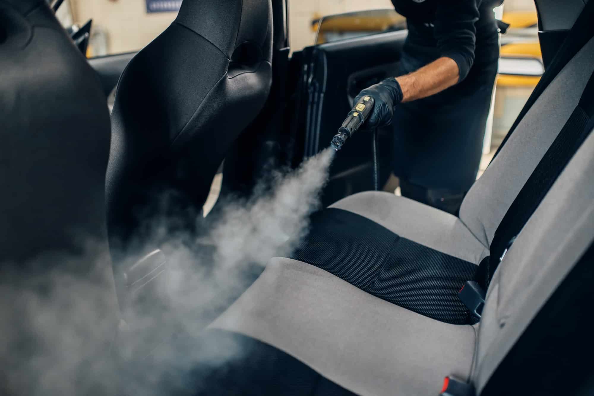 carwash worker cleans seats with steam cleaner